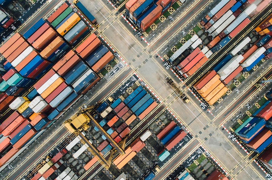 Aerial view of a container yard with several red automated guided vehicles transporting cargo containers numbered 825, 811, 855, and 711.